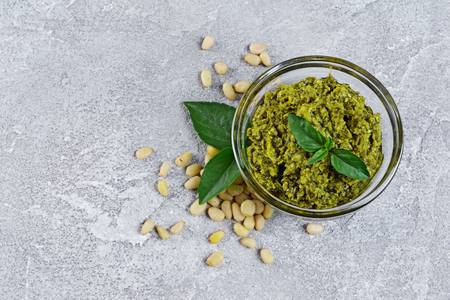 Traditional italian green sauce pesto in glass bowl with pine nuts and basil leaves on gray concrete backgroundの写真素材