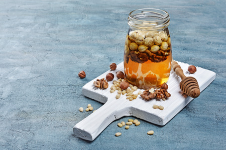 Healthy mix of natural honey with different nuts in a jar and wooden dipper on white board and blue concrete backgroundの写真素材