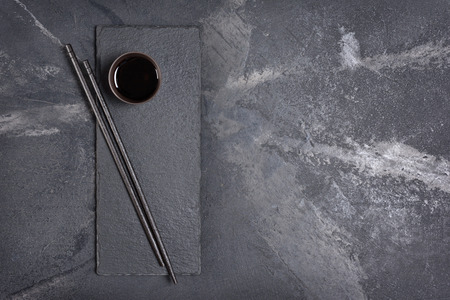 Dark bowl of asian salty soy sauce with wooden chopsticks on black slate board and marble backgroundの写真素材