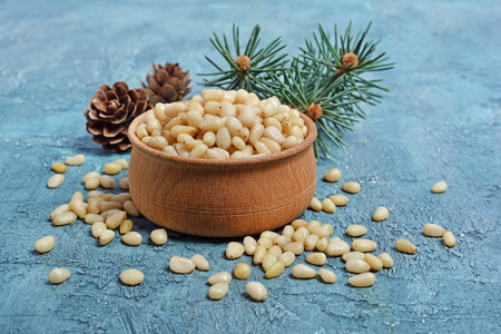 Closeup on healthy and tasty pine nuts in small wooden rustic bowl with cedar bump and branch on blue concrete backgroundの写真素材