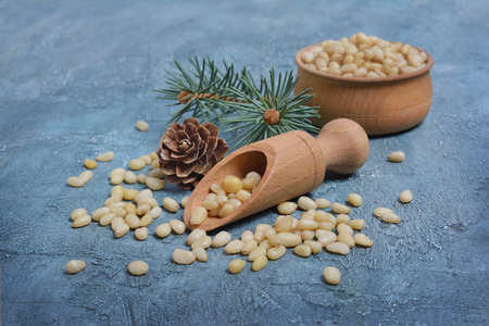 Closeup on healthy and tasty pine nuts in small wooden rustic bowl with wood scoop and cedar bump on blue concrete backgroundの写真素材