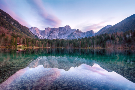 Beautiful sunset landscape of Lago or Laghi di Fusine lake in Italy with spruces on shore on blue sky and mountains backgroundの写真素材