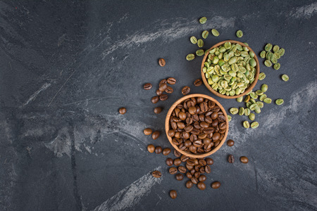 Top view of raw green and brown roasted coffee beans in wooden bowls on black marble background with copy spaceの写真素材