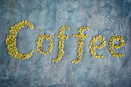 Top view of lettering with raw green coffee beans on blue concrete backgroundの写真素材