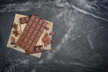Top view of spicy dark chocolate bars with cocoa beans and anise stars on parchment paper and black...
