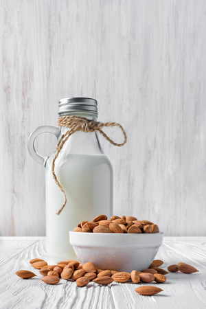 Healthy natural almond milk in glass bottle with nuts in bowl for vegan and vegetarian on white wooden backgroundの写真素材