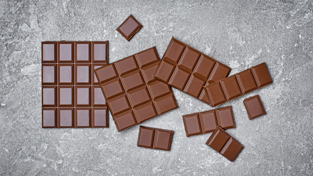 Top view of tasty broken chocolate bars as snack or ingredient for confectionery on gray concrete...