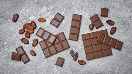 Top view of tasty broken chocolate bars with cocoa beans as ingredient for confectionery on gray concrete backgroundの写真素材