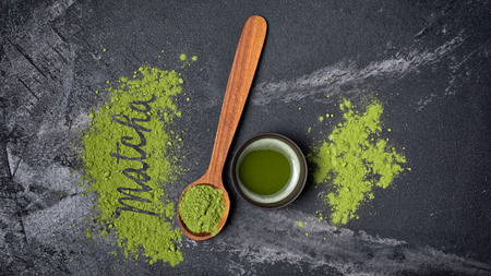 Top view on organic green matcha tea in ceramic cup with wooden spoon on black marble background