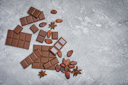 Top view of tasty broken chocolate bars with cocoa beans and anise stars as ingredient for confectionery on gray concrete background with copy spaceの写真素材