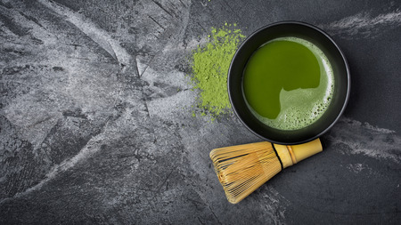 Top view on organic green matcha tea in ceramic cup with bamboo whisk on black marble background with copy spaceの写真素材
