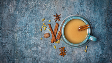 Top view on traditional Indian drink masala chai tea with milk and cinnamon stick, green cardamom, anise star and nutmeg on blue concrete background with copy spaceの写真素材