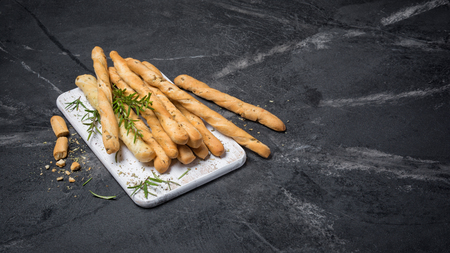 Traditional Italian appetizer grissini with rosemary spice on white wooden board on black marble background with copy spaceの写真素材