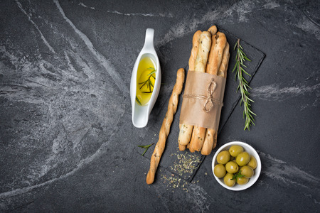 Top view of traditional italian appetizer grissini with rosemary spice and olive oil in sauceboat on black slate board and marble background with copy spaceの写真素材