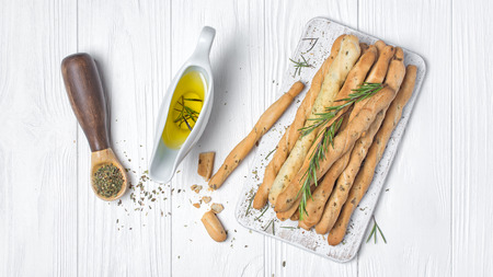 Top view of traditional italian appetizer grissini with rosemary spice in spoon and olive oil in...