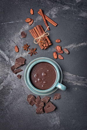 Top view on homemade spicy hot chocolate in ceramic cup with cinnamon stick, anise stars, dark chocolate pieces and cocoa beans on black marble backgroundの写真素材