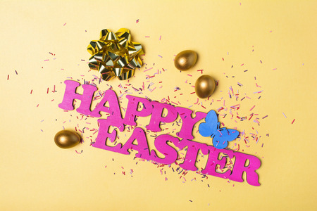 Top view on pink text of happy Easter and golden painted eggs with bright colorful sugar sprinkles...