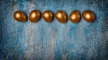 Top view on shiny painted golden eggs as symbol of Easter on blue concrete background with copy spaceの写真素材