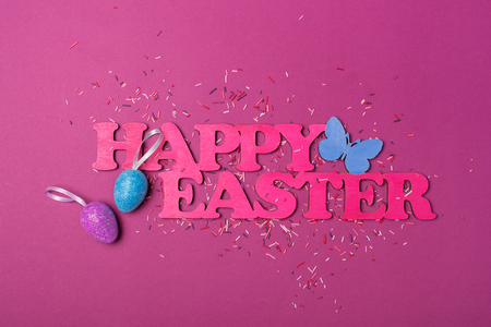 Top view on pink text of happy Easter and glittering eggs with bright colorful sugar sprinkles or confetti as baking decor on purple backgroundの写真素材