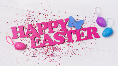 Top view on pink text of happy Easter and glittering eggs with bright colorful sugar sprinkles or confetti as baking decor on white wooden backgroundの写真素材