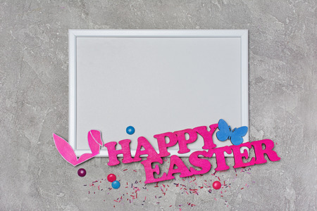 Top view on mockup of blank white frame with pink text of happy easter and bunny ears on gray concrete backgroundの写真素材