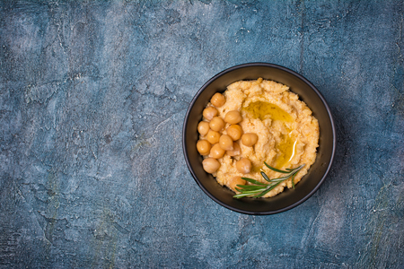 Traditional chickpea hummus snack with spice of rosemary in black bowl on blue concrete background with copy spaceの写真素材