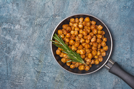 Roasted salty and spicy chickpeas in frying pan with rosemary on blue concrete background with copy spaceの写真素材