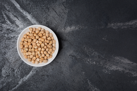 Raw chickpeas in white bowl as ingredient for vegetarian dish on black marble background with copy spaceの写真素材