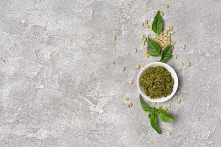 Top view of pesto sauce in bowl with ingredients as pine nuts and basil leaves on gray concrete background with copy spaceの写真素材