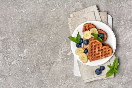 Top view of belgian waffles with fresh blueberries and bananas on gray concrete background with copy spaceの写真素材