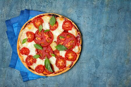 Top view of round pizza margarita with tomato, cheese and basil leaves for vegetarians on blue concrete background with copy spaceの写真素材