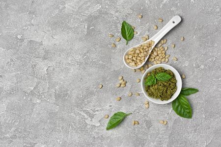 Top view of pesto sauce in bowl with ingredients as pine nuts and basil leaves on gray concrete background with copy spaceの写真素材