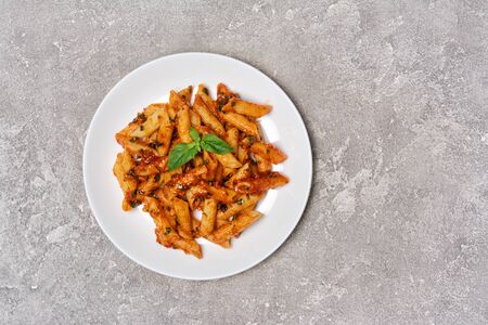 Plate of arrabiata pasta with fresh basil leaves on gray concrete background with copy spaceの写真素材