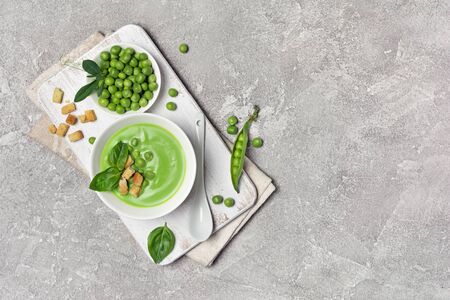 Top view of light summer soup of young green peas with basil leaves and croutons on gray concrete background with copy spaceの写真素材
