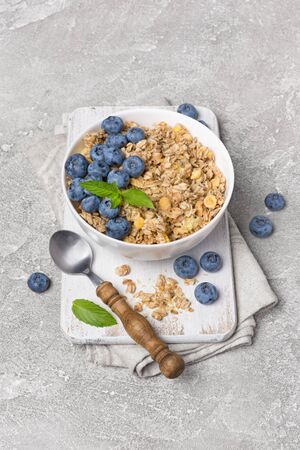 Oatmeal or granola with fresh blueberry in white bowl for healthy breakfast on wooden board and gray concrete backgroundの写真素材