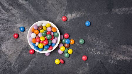 Chocolate multicolored glaze dragee or candies in white bowl on black marble background with copy spaceの写真素材