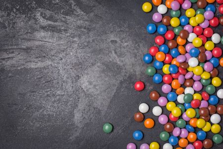 Chocolate multicolored glaze dragee or candies on black marble background with copy space