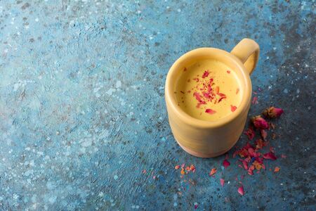 Top view of golden turmeric milk with spices in big cozy mug for healthy life on blue concrete background with copy spaceの写真素材