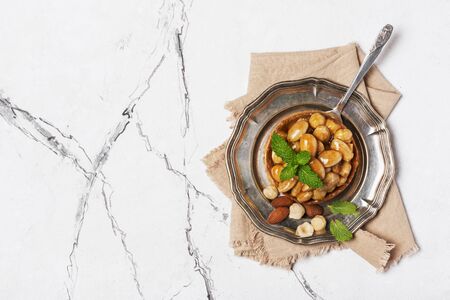 Top view of tasty nutty dessert on vintage silver tray with fresh green mint on white marble background with copy spaceの写真素材
