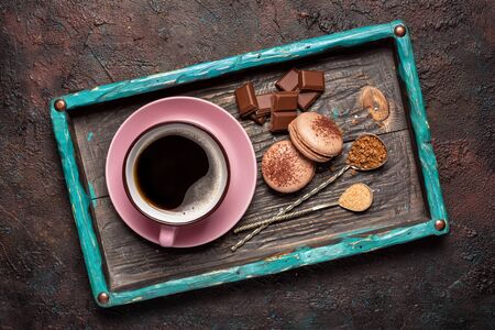 Top view of french dessert macaroons with chocolate and pink cup of coffee on wooden tray and dark background with copy spaceの写真素材
