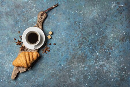 Top view of traditional french breakfast with croissant and coffee on wooden board and blue concrete background with copy spaceの写真素材