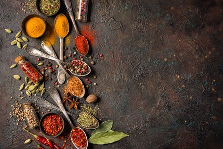 Top view of mix bright spices in vintage silver spoons, bowls and vials as ingredient for healthy food on brown grunge background with copy space