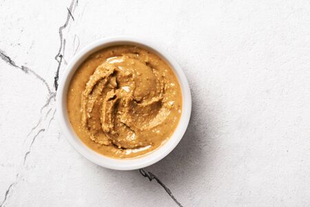 Top view of peanut butter in white bowl on marble background