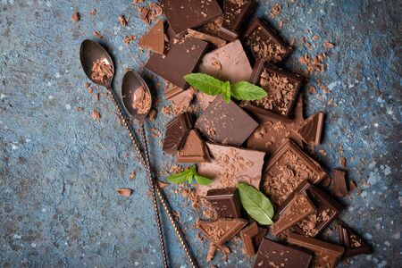 Top view of broken tasty milk and dark chocolate bars with fresh green mint and two long cocktail...