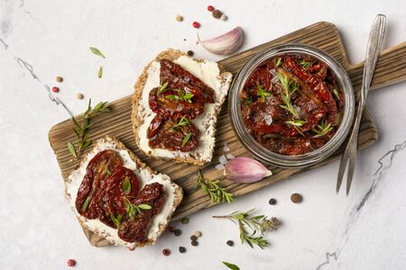 Top view of sandwich with bread, soft cheese and homemade sun-dried tomatoes with green herbs, garlic and spices in olive oil on white marble backgroundの写真素材