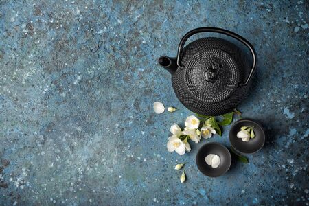Top view of asian black traditional kettle and cups with healthy green jasmine tea on blue concrete background with copy spaceの写真素材