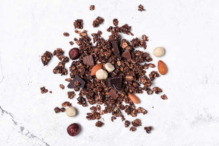 Top view of oatmeal or granola with pieces of dark chocolate, almond and hazelnut for nutritious breakfast on white marble backgroundの写真素材