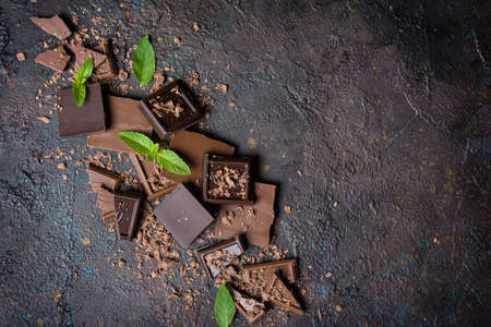 Top view of broken tasty milk and dark chocolate bars with fresh green mint on brown concrete background with copy spaceの写真素材
