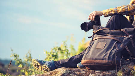 Young adult in shirt with dark gray backpack holding a camera for landscape photography. Travel conceptの写真素材