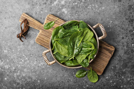 Top view of vintage baking dish with green fresh baby spinach on wooden board and gray concrete backgroundの写真素材